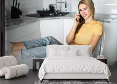 Portrait of young woman talking cell phone, drink coffee or tea in the kitchen Wall mural